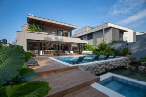 Fachada moderna de mansão com piscina, deck de madeira, área gourmet e lago ornamental integrado ao paisagismo.
