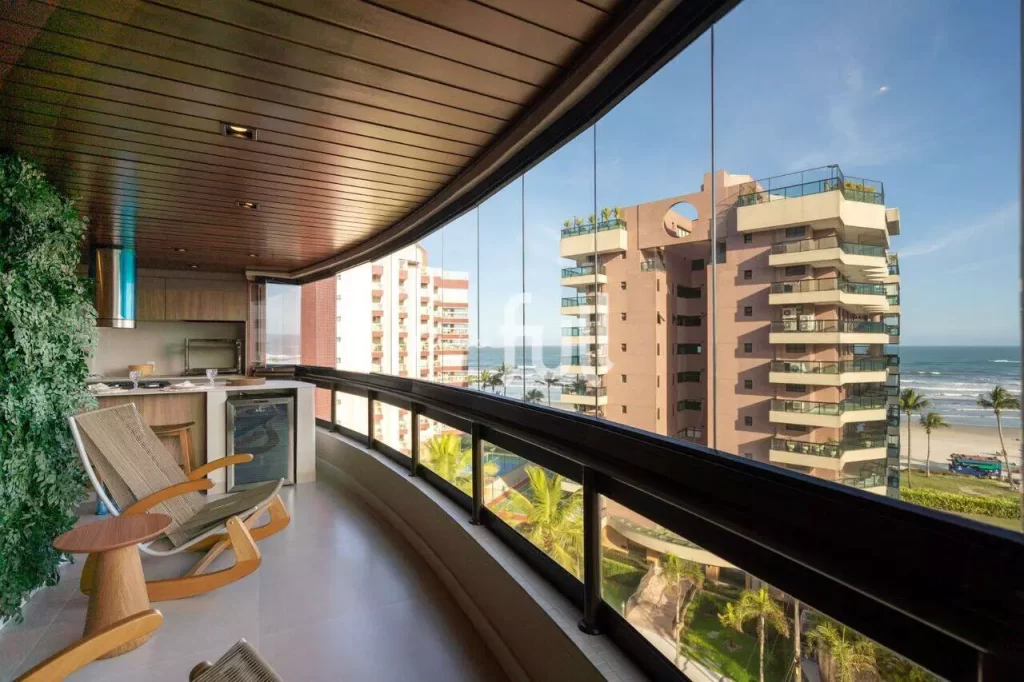 Varanda gourmet moderna com fechamento em vidro e vista para o mar e prédios.