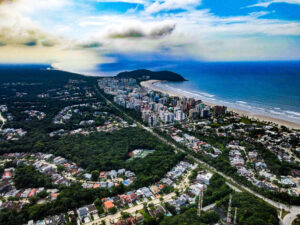 Vista aérea da Riviera de São Lourenço, com prédios à beira-mar, faixa de areia extensa, mar azul e áreas residenciais cercadas por vegetação.
