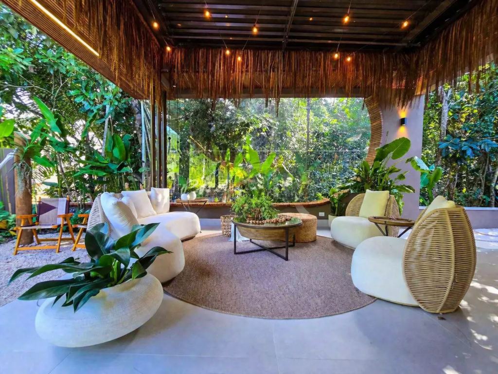 Área de estar integrada ao jardim com decoração tropical e móveis orgânicos.