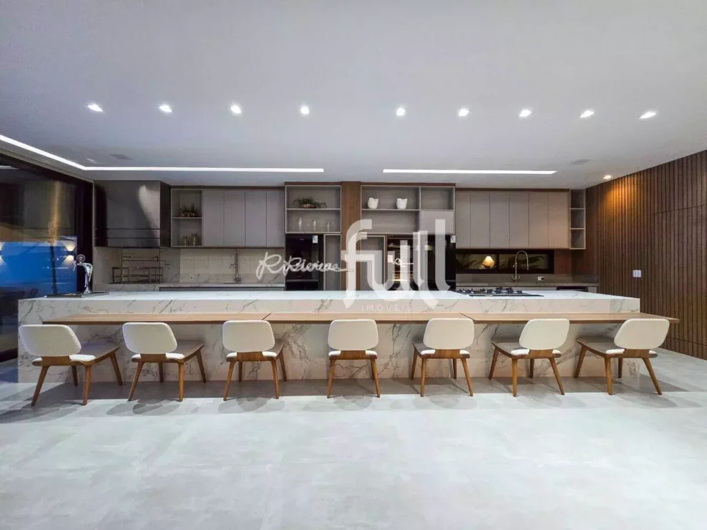 Cozinha gourmet moderna com ampla bancada em pedra, cadeiras alinhadas e iluminação embutida no teto.