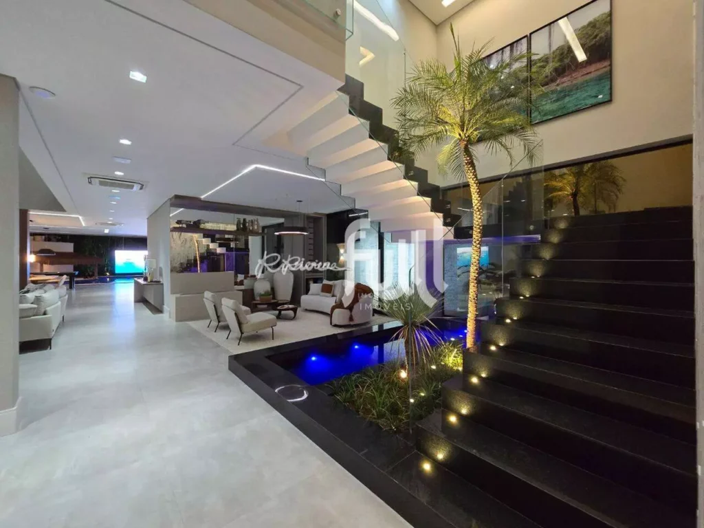 Hall de entrada luxuoso com escada suspensa, jardim interno iluminado e ambientes integrados de estar e convivência.